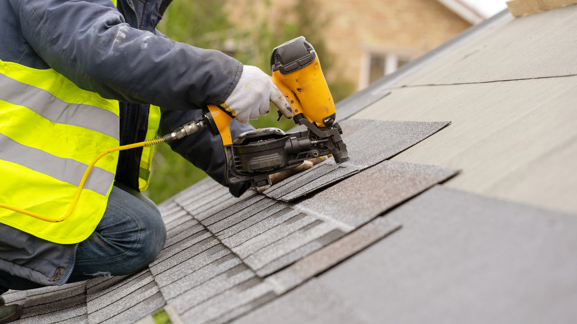 A man wearing a safety vest is diligently working on a roof, ensuring safety and precision in his task.